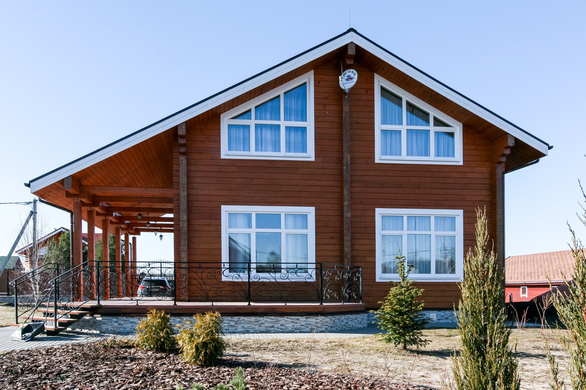 Фасад двухэтажного деревянного дома из клееного бруса орехового цвета с террасой и белыми окнами