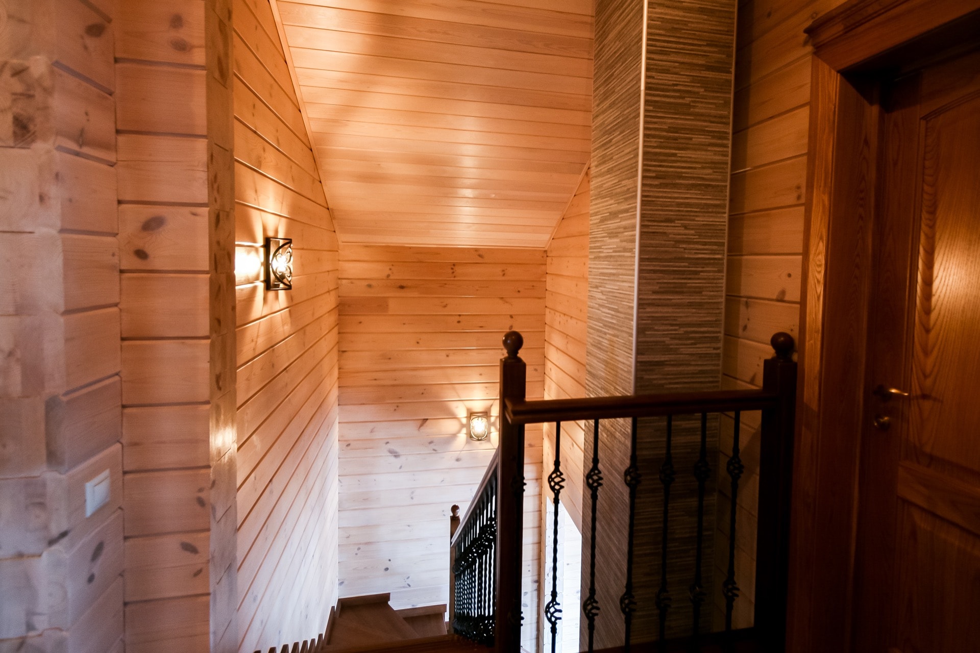 Лестничный холл в деревянном доме из клееного бруса с установленными светильниками и дымоходом